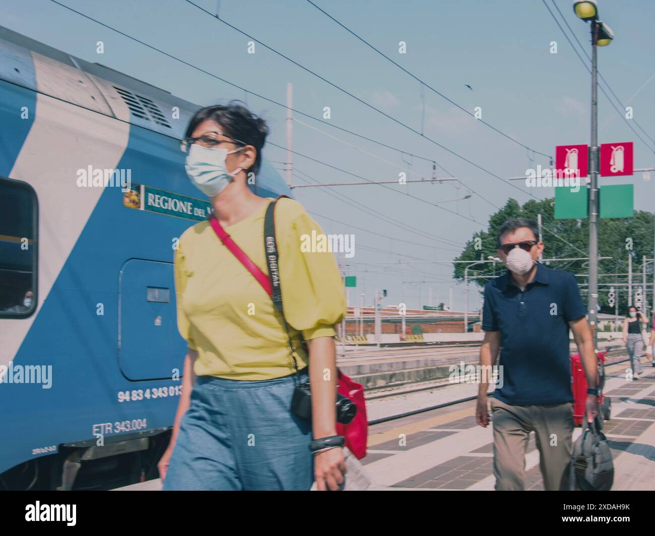Passeggeri che indossano maschere che camminano su un binario ferroviario con un treno blu sullo sfondo, Venezia, Italia, 30 giugno 2020 Foto Stock