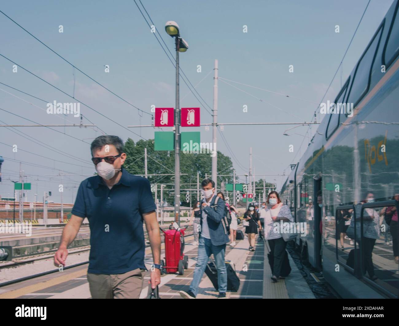 Passeggeri che indossano maschere su un binario ferroviario con un treno presente sullo sfondo, Venezia, Italia, 30 giugno 2020 Foto Stock