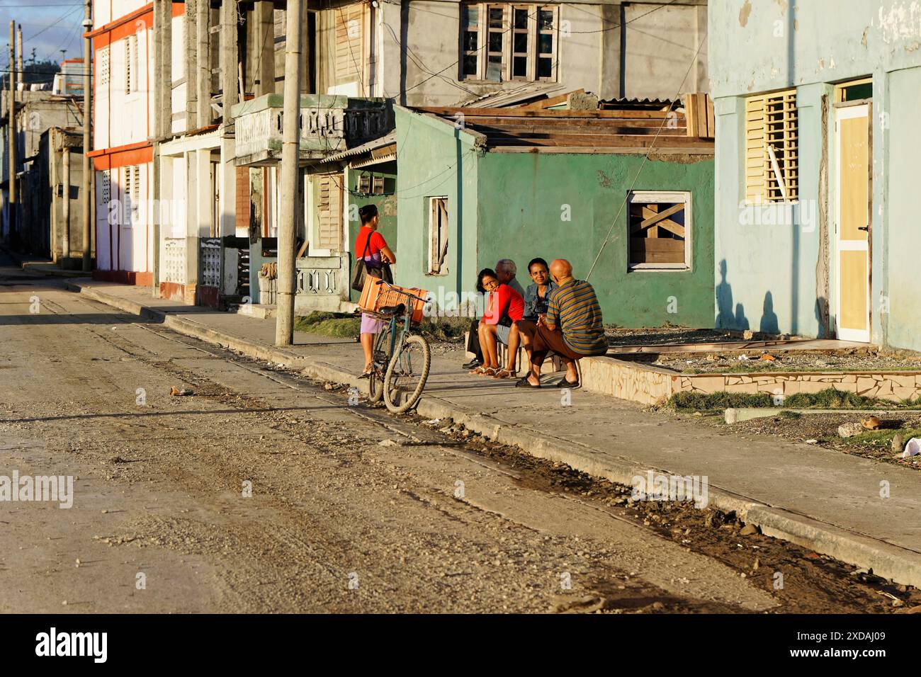 Baracoa, Cuba, America centrale, alcune persone si siedono e parlano su un marciapiede vicino a vecchi edifici, una bicicletta si appoggia contro un muro, Cuba Foto Stock