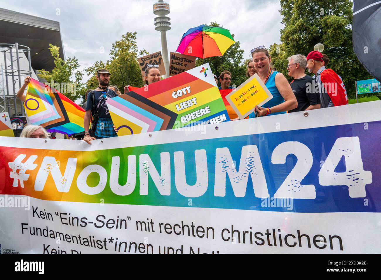 Queerer protesta gegen die UNUM24 Glaubenskonferenz, Die in der Olympiahalle stattfindet, München, 21. Juni 2024 Deutschland, München, 21. Juni 2024, Queerer protesta gegen die UNUM24 Glaubenskonferenz, Die in der Olympiahalle stattfindet, Teilnehmer mit T-Shirt-Aufschrift: Queer, geliebt, gesegnet, TeilnehmerInnen demonstrieren am Brundageplatz am Olympiazentrum gegen die christlich-konative Eins sein Konein Konein Demo 24 überkonfessionelle. Juni 2024, motto Einssein, lateinisch UNUM, hier im Hintergrund der Foto Stock