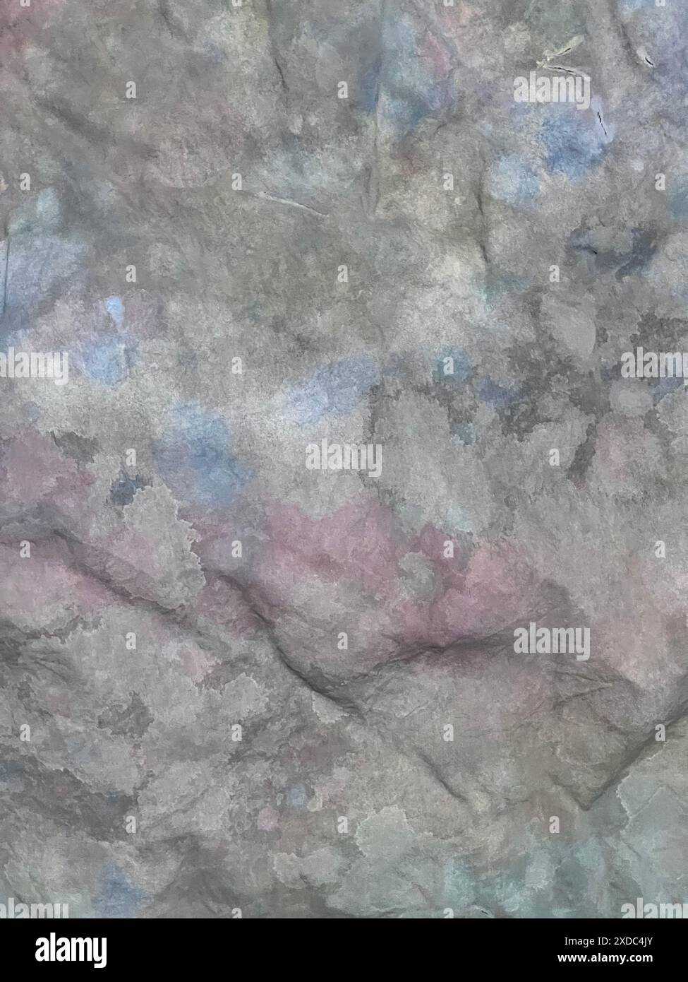 Immagine ravvicinata di una superficie rocciosa grigia e ruvida con sottili macchie blu e rosa. La roccia ha una consistenza naturale con piccole crepe e fessure. L'im Foto Stock