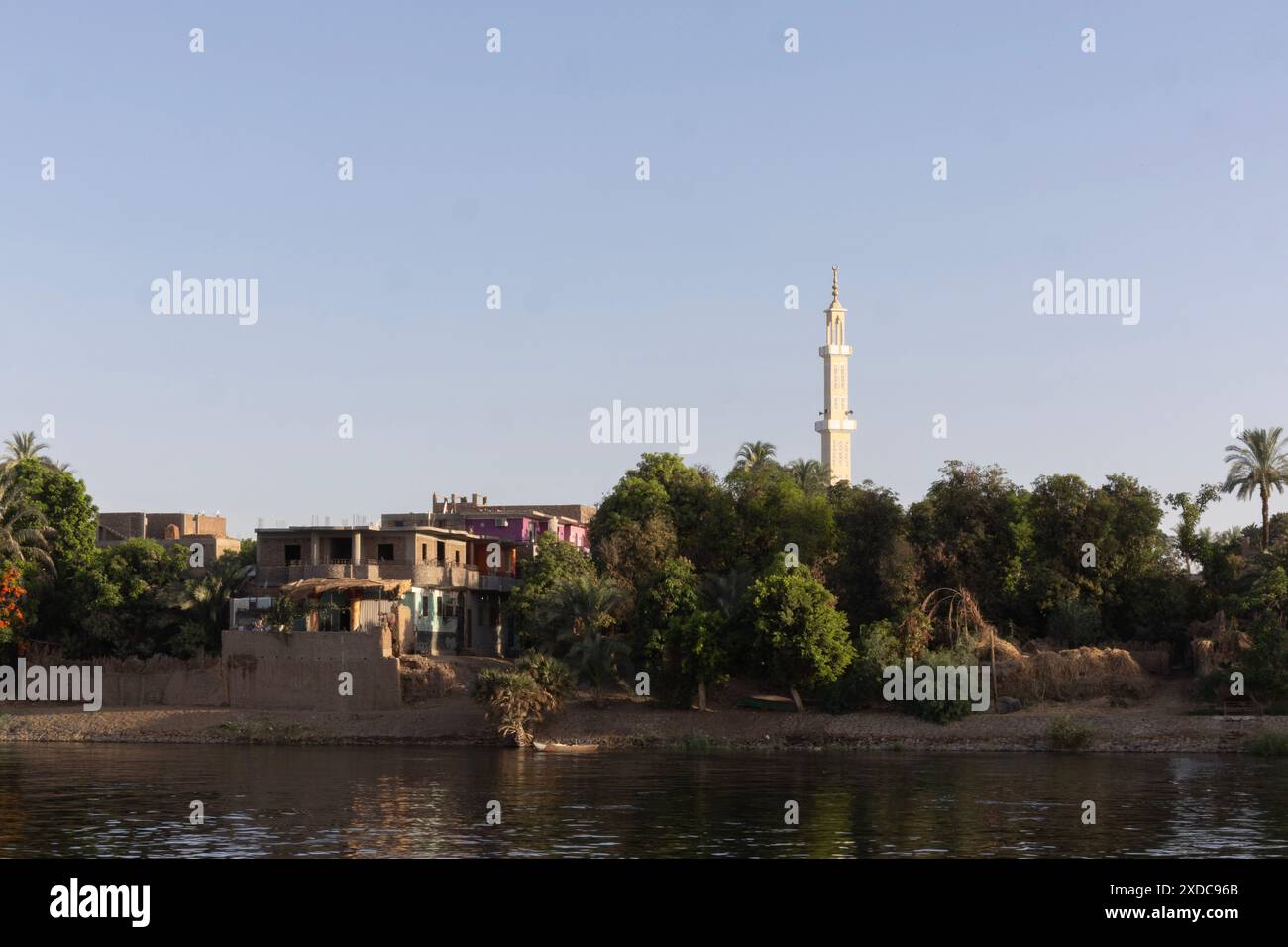 Case dai colori vivaci in un villaggio dominato da un minareto visto al sole della mattina presto lungo il fiume Nilo tra Esna e El-Kab, Egitto. Foto Stock