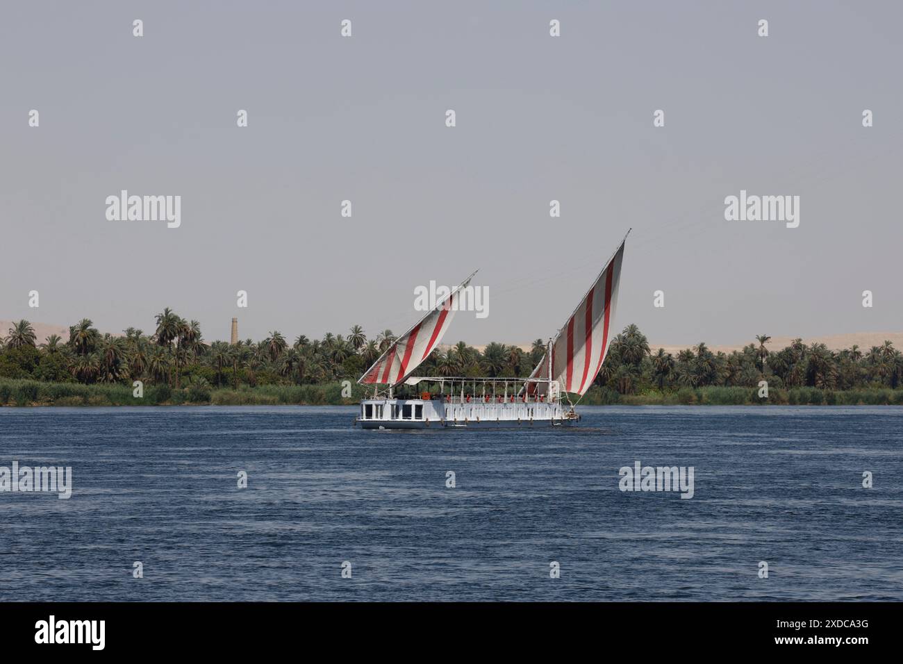 Una barca a vela dahabiya con vela latina a strisce rosse/bianche naviga tranquillamente lungo il fiume Nilo tra Luxor e Assuan in Egitto. Foto Stock