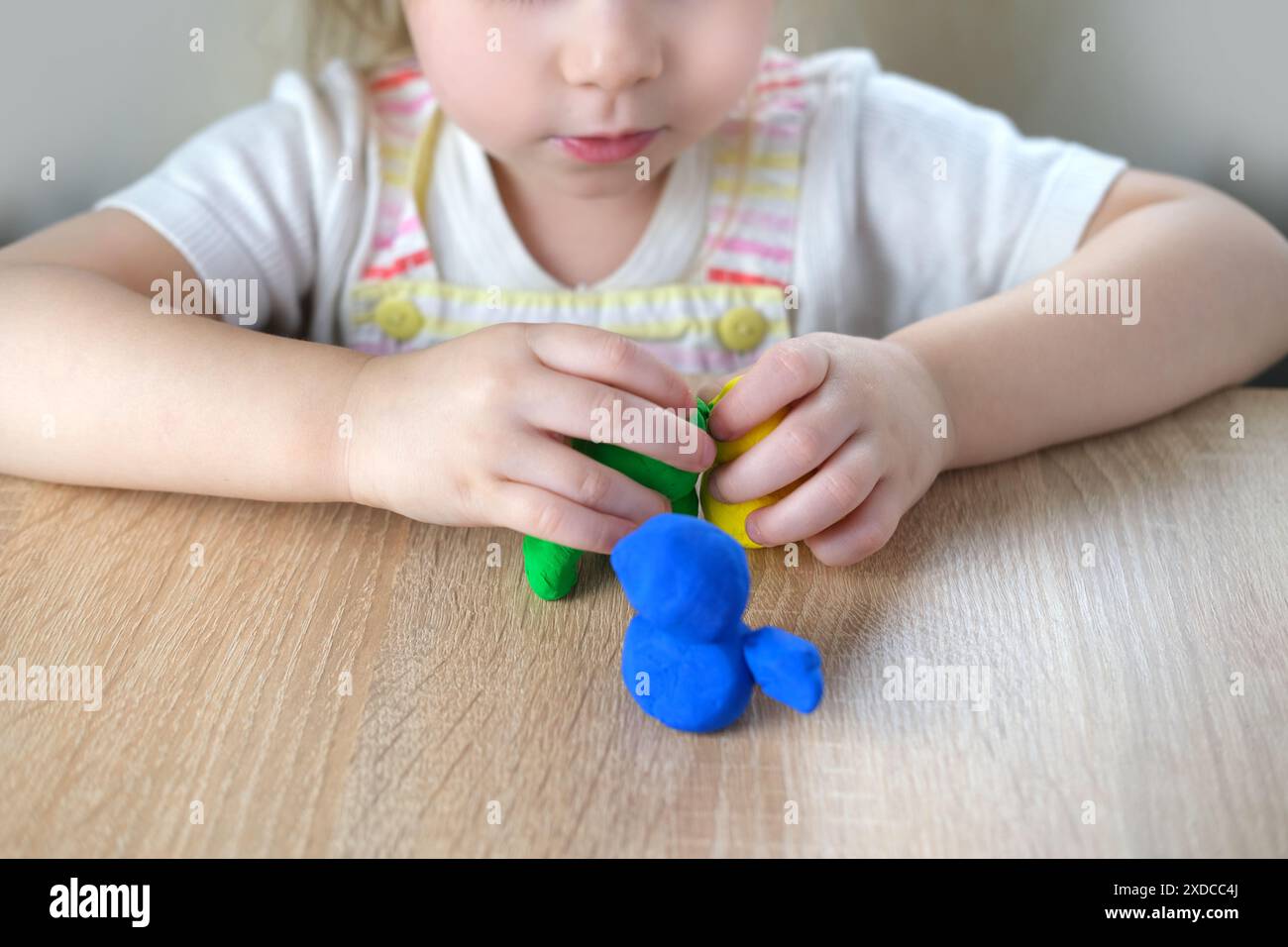 giocattoli in plastica per primi piani nelle mani di bimbi piccoli, bimbi piccoli, bionda di 2 anni scolpisce figure di personaggi di impasto colorato, concetto di fine m Foto Stock