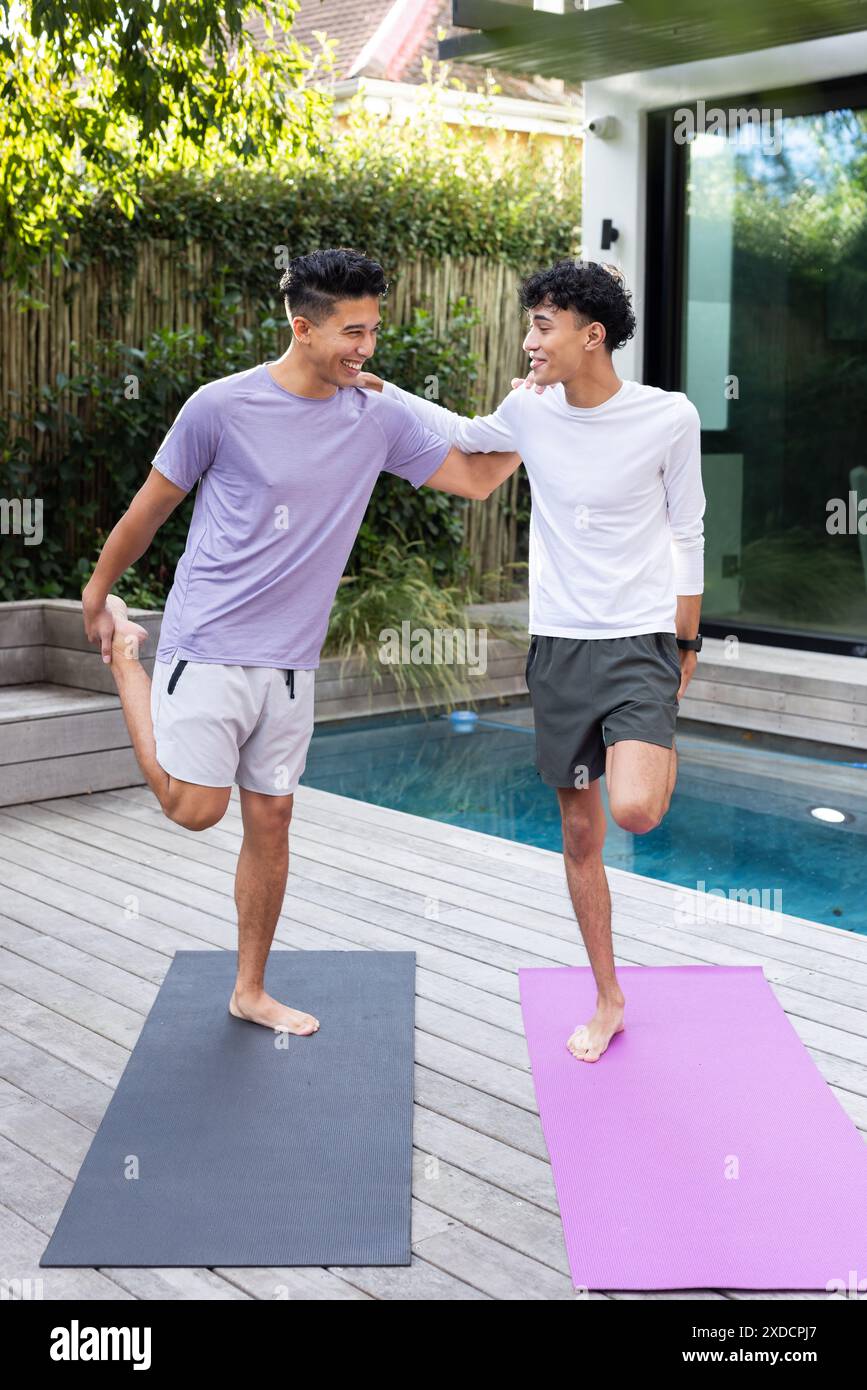 Stretching su tappetini da yoga, amici maschi che sorridono l'un l'altro Foto Stock