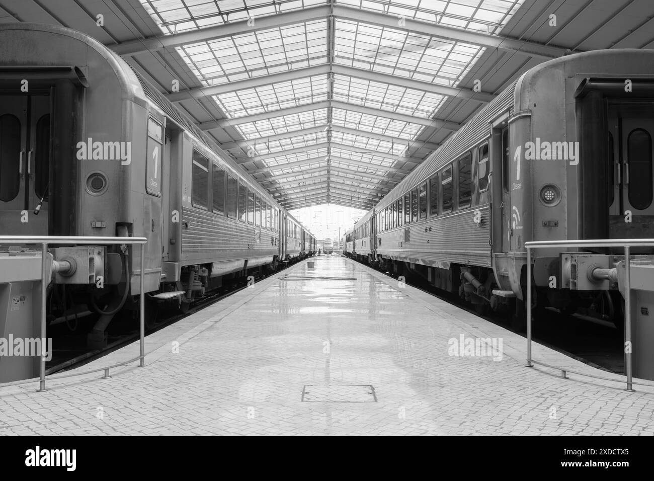 I moderni treni passeggeri si trovano sotto il tetto di una stazione ferroviaria di Lisbona. Stazione coperta e treni che guardano in lontananza. ima in bianco e nero Foto Stock