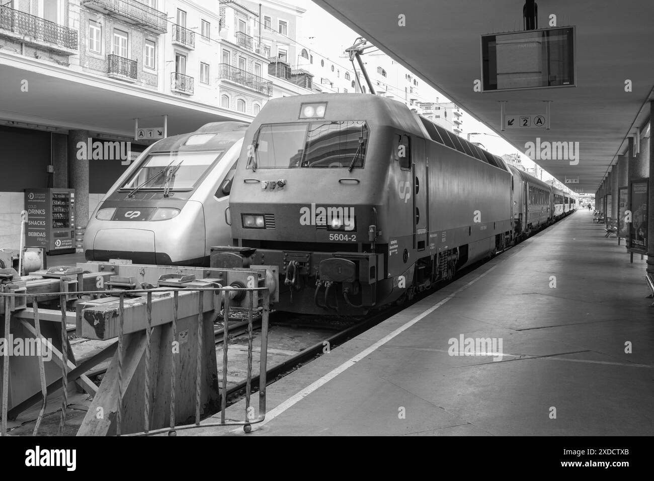 I moderni treni passeggeri si trovano sotto il tetto di una stazione ferroviaria di Lisbona. Stazione coperta e treni che guardano in lontananza. ima in bianco e nero Foto Stock