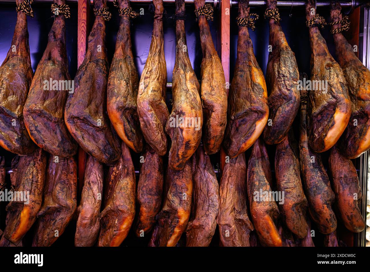 Vendere jamon sul mercato. Il prosciutto sotto forma di mozziconi di maiale è appeso al bancone, in attesa dei clienti. Prodotto nazionale della Spagna. Foto Stock