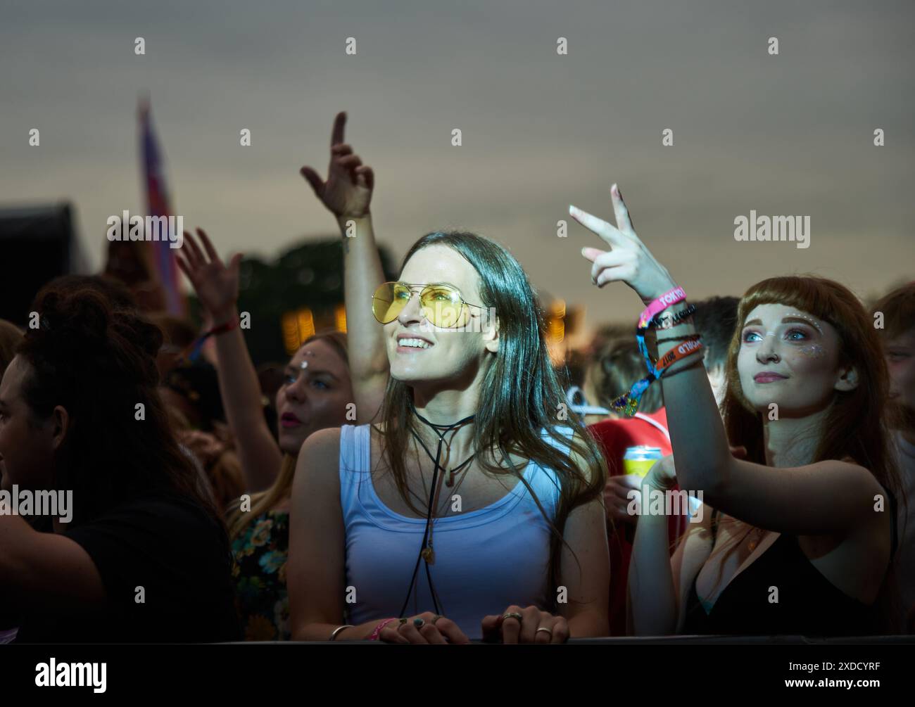 la ragazza con gli occhiali da sole gialli sorride mentre viene catturata sotto i riflettori guardando una band ad un festival in estate Foto Stock