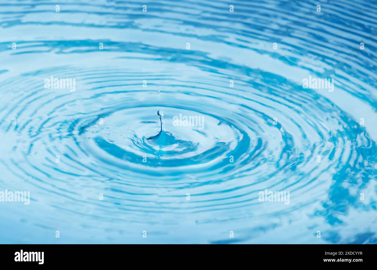 Una goccia di pioggia cade nell'acqua e lascia dei cerchi sulla superficie Foto Stock