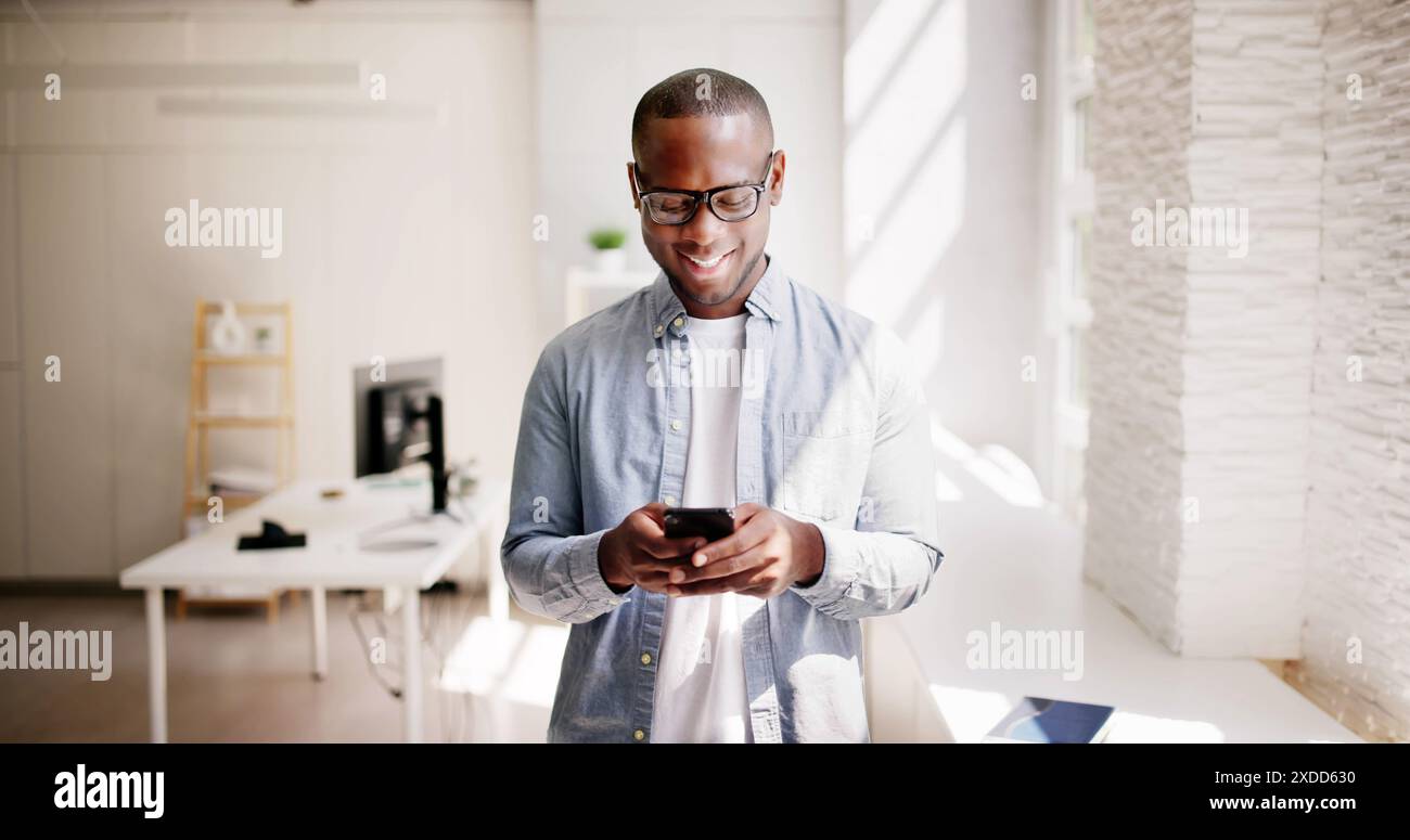 Un uomo d'affari afro-americano gestisce con competenza le vendite tramite un'app per smartphone, fornendo un servizio clienti di prim'ordine in un ambiente moderno. Foto Stock