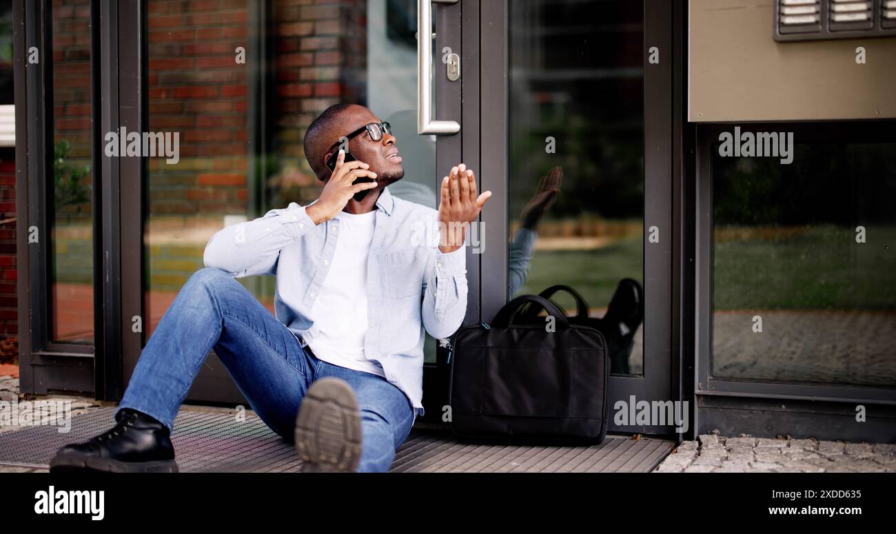 Frustrato uomo afroamericano chiuso fuori casa, aspetta Locksmith, utilizza l'app smartphone per l'assistenza di accesso. Foto Stock