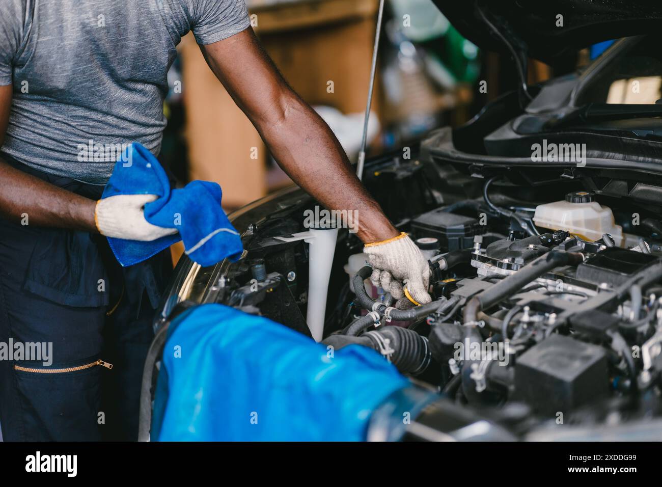 Garage Mechanic African Black maschio lavoro auto auto di lavoro professionale che controlla l'olio motore sul cofano anteriore. Foto Stock
