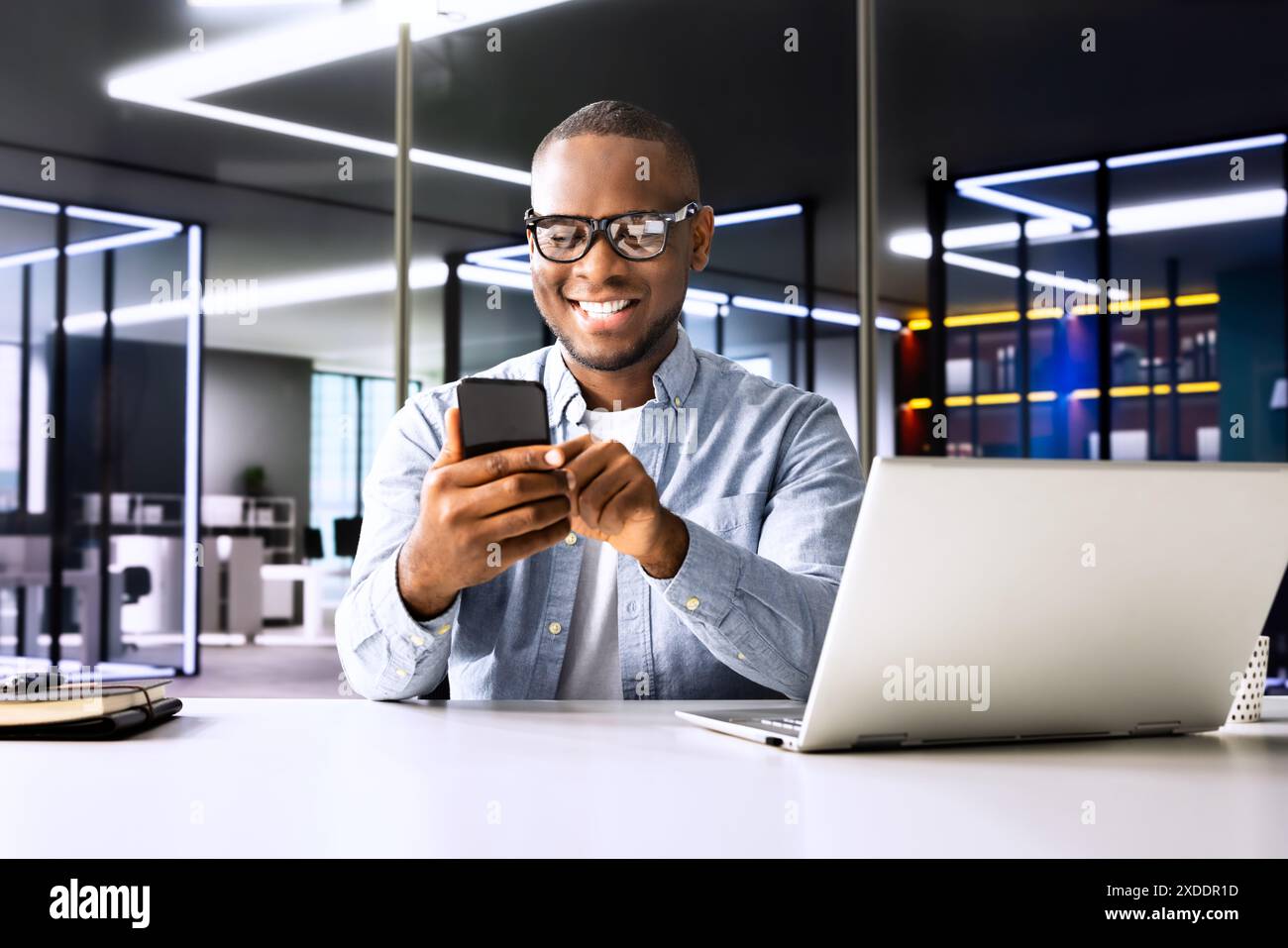 Il consulente di marketing digitale moderno: Giovane afroamericano sorridente mentre invia SMS su smartphone in ufficio Foto Stock