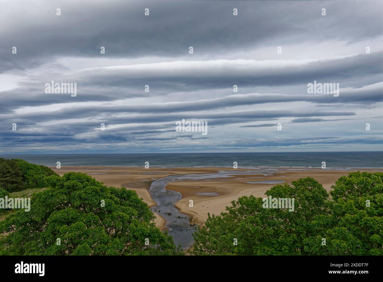 La foce del fiume Lunan che scorre nel Mare del Nord sopra la grande distesa di sabbia esposta durante la bassa marea sotto tempesta scura nuvole. Foto Stock