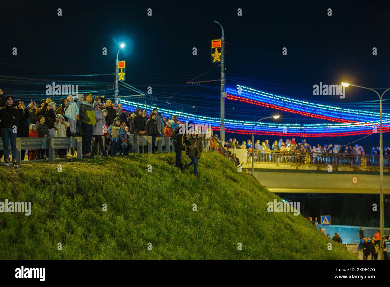La folla di russi sulla strada sulla collina e sul ponte sta guardando i fuochi d'artificio in un cielo notturno Foto Stock
