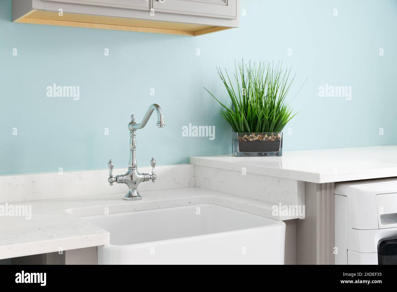 Un rubinetto e un lavabo in grembiule con pareti blu, ripiani e elettrodomestici in marmo bianco e armadi marroni. Foto Stock