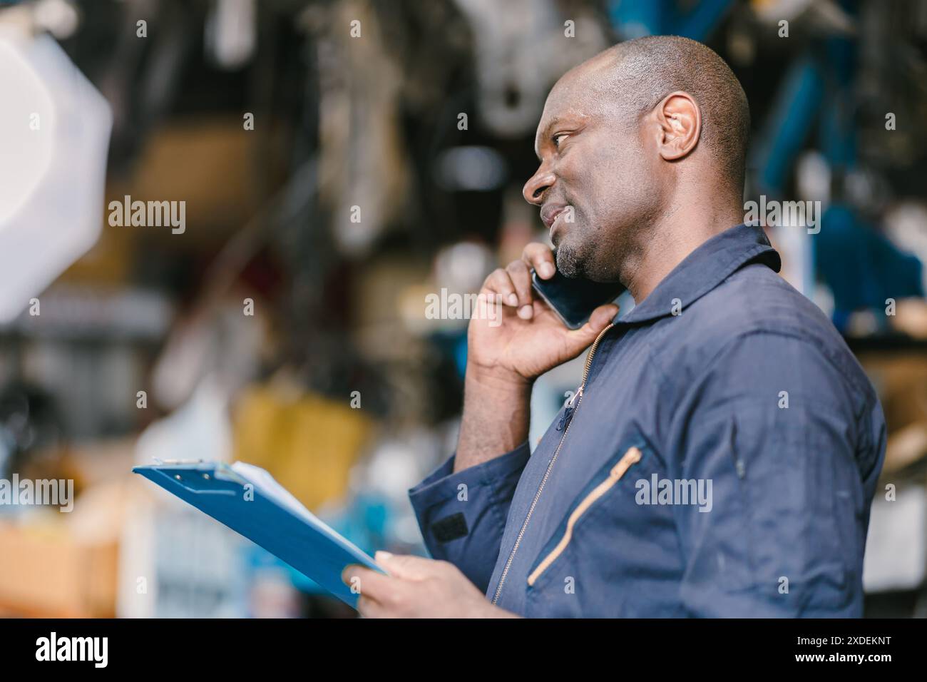 Responsabile tecnico del lavoratore del garage che parla telefonicamente con il cliente per informazioni sull'assistenza. Foto Stock