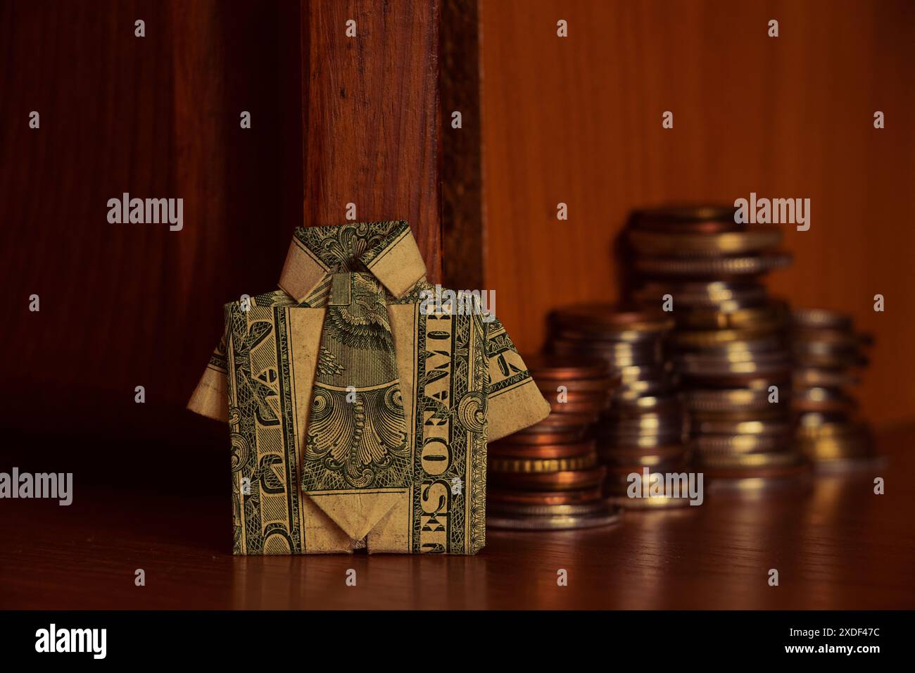 Una camicia fatta di banconota da un dollaro e una pila di monete si stagliano su un armadietto di legno, affari e finanza, dollaro Foto Stock