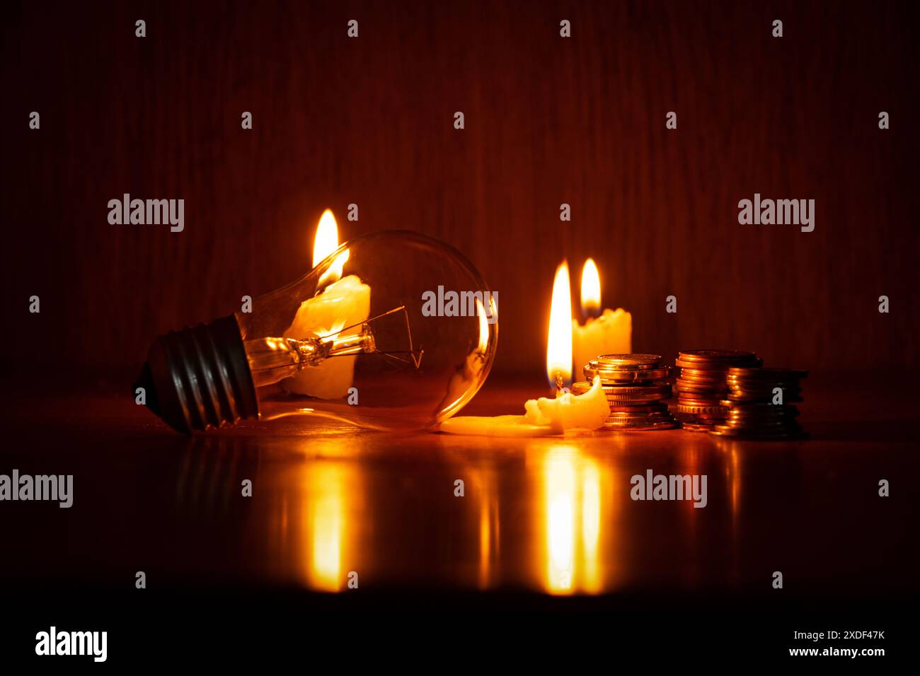 Lampada a incandescenza, candela e pile di monete al buio a casa, niente luce, niente soldi Foto Stock