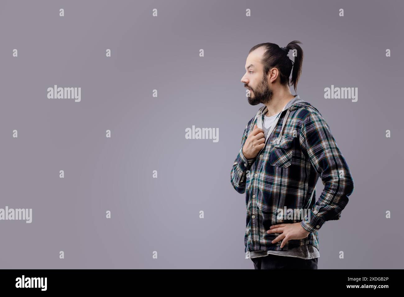 L'uomo preoccupato con la barba e la coda di cavallo tocca il petto, mostrando sorpresa e dolore, accennando a un timore per la salute Foto Stock