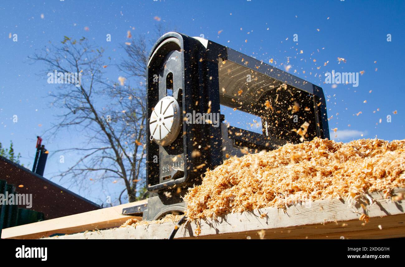 La segatura viene dispersa nell'aria quando un 2x4 attraversa una levigatrice industriale in un cantiere edile di giorno. Foto Stock