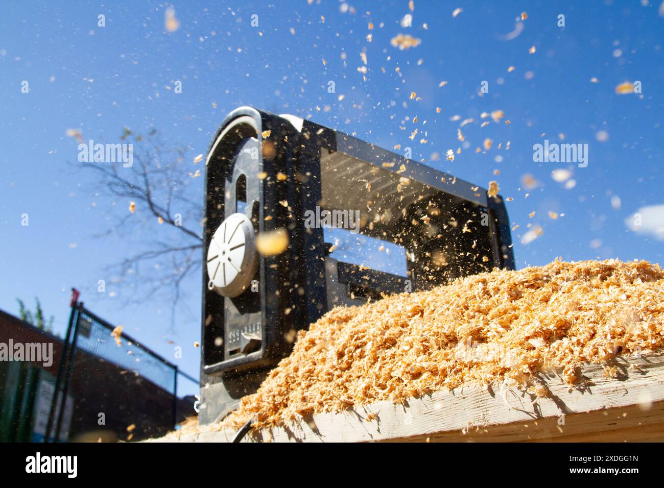 La segatura viene dispersa nell'aria quando un 2x4 attraversa una levigatrice industriale in un cantiere edile di giorno. Foto Stock
