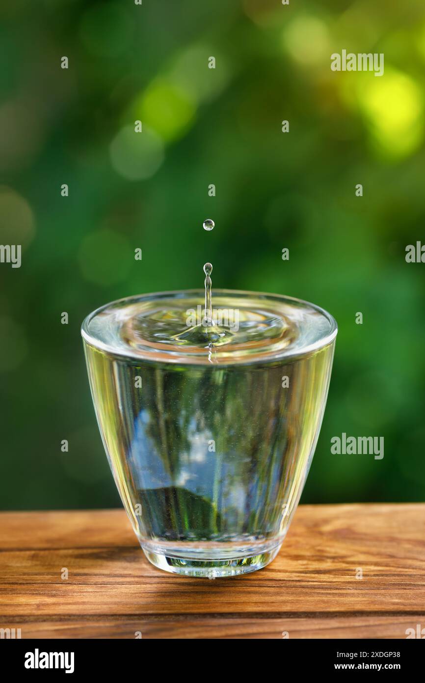 bicchiere d'acqua con spruzzi e caduta su un tavolo di legno Foto Stock