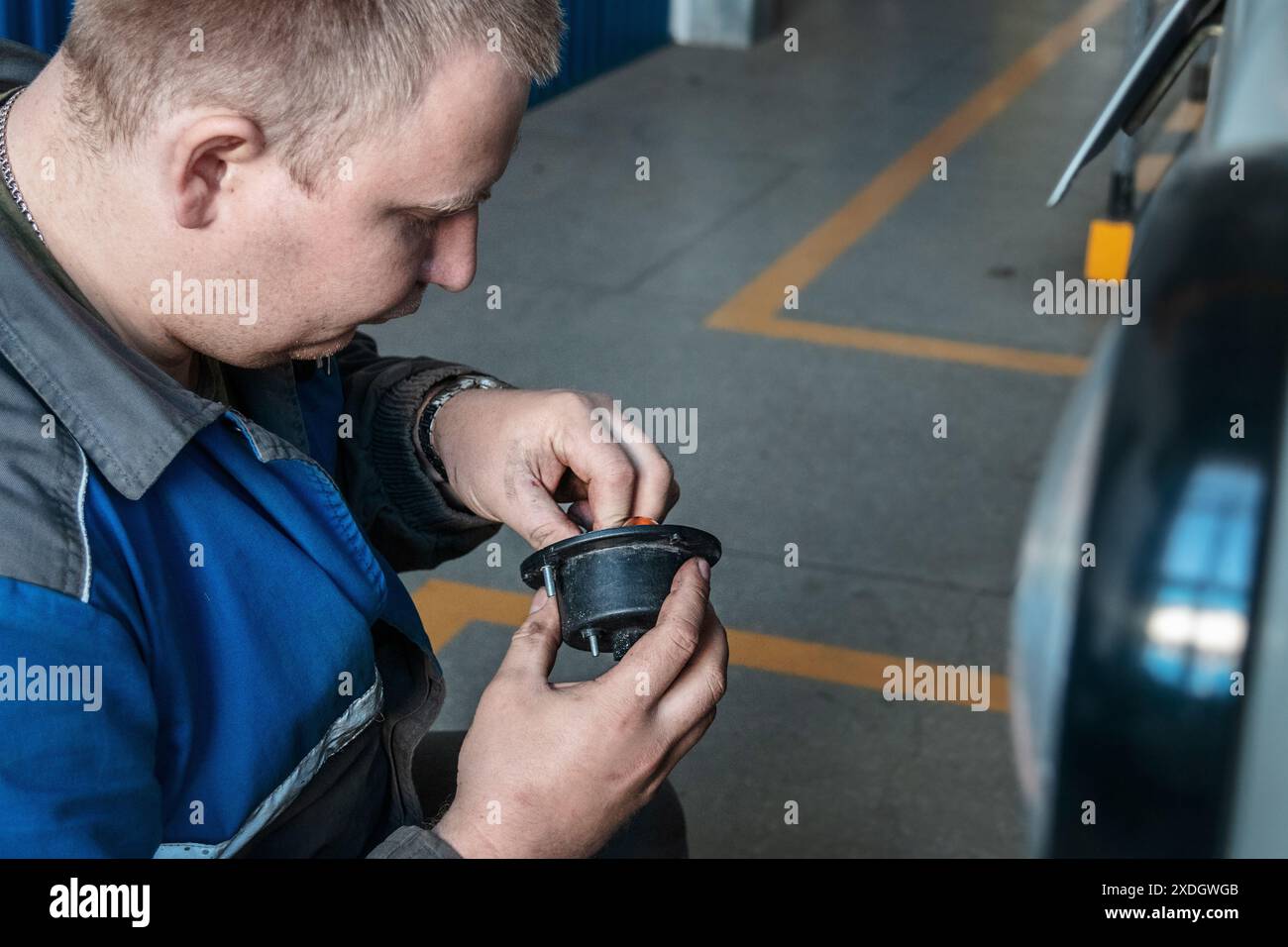 Un uomo sta lavorando al motore di un'auto. Indossa una camicia blu e una giacca grigia Foto Stock