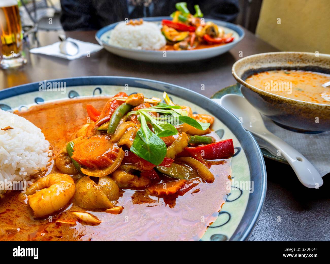 Salsa al curry rosso con gamberetti e verdure su due piatti, zuppa nel recipiente e birra sul tavolo. Cucina asiatica. Foto Stock