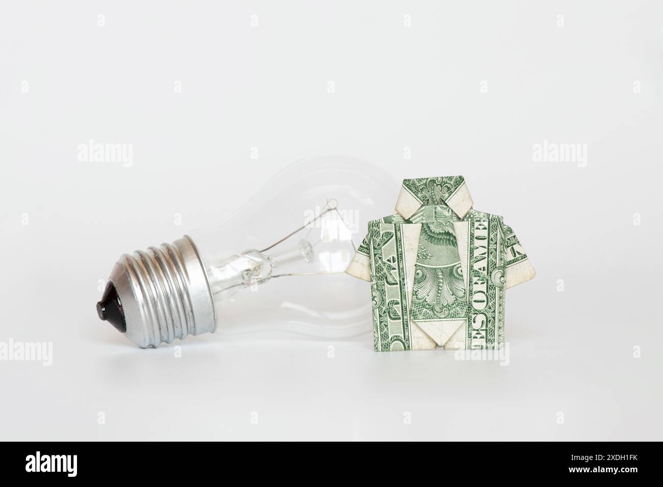 Camicia da un dollaro e lampada a incandescenza su sfondo bianco, prezzo leggero e tariffa, denaro Foto Stock