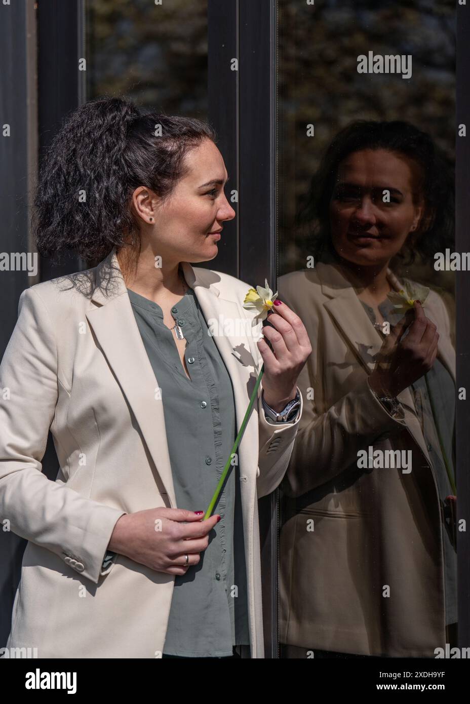 Una giovane donna felice cammina per la città, guarda fuori da un'enorme finestra, tiene un narcidio nelle sue mani. Positivo, atmosfera primaverile Foto Stock