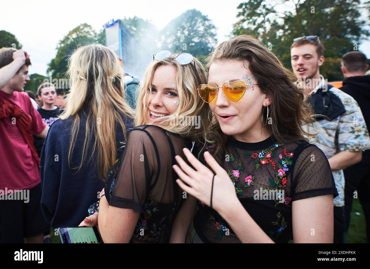 due belle ragazze ballano in mezzo alla folla al festival, una indossa occhiali da sole Foto Stock