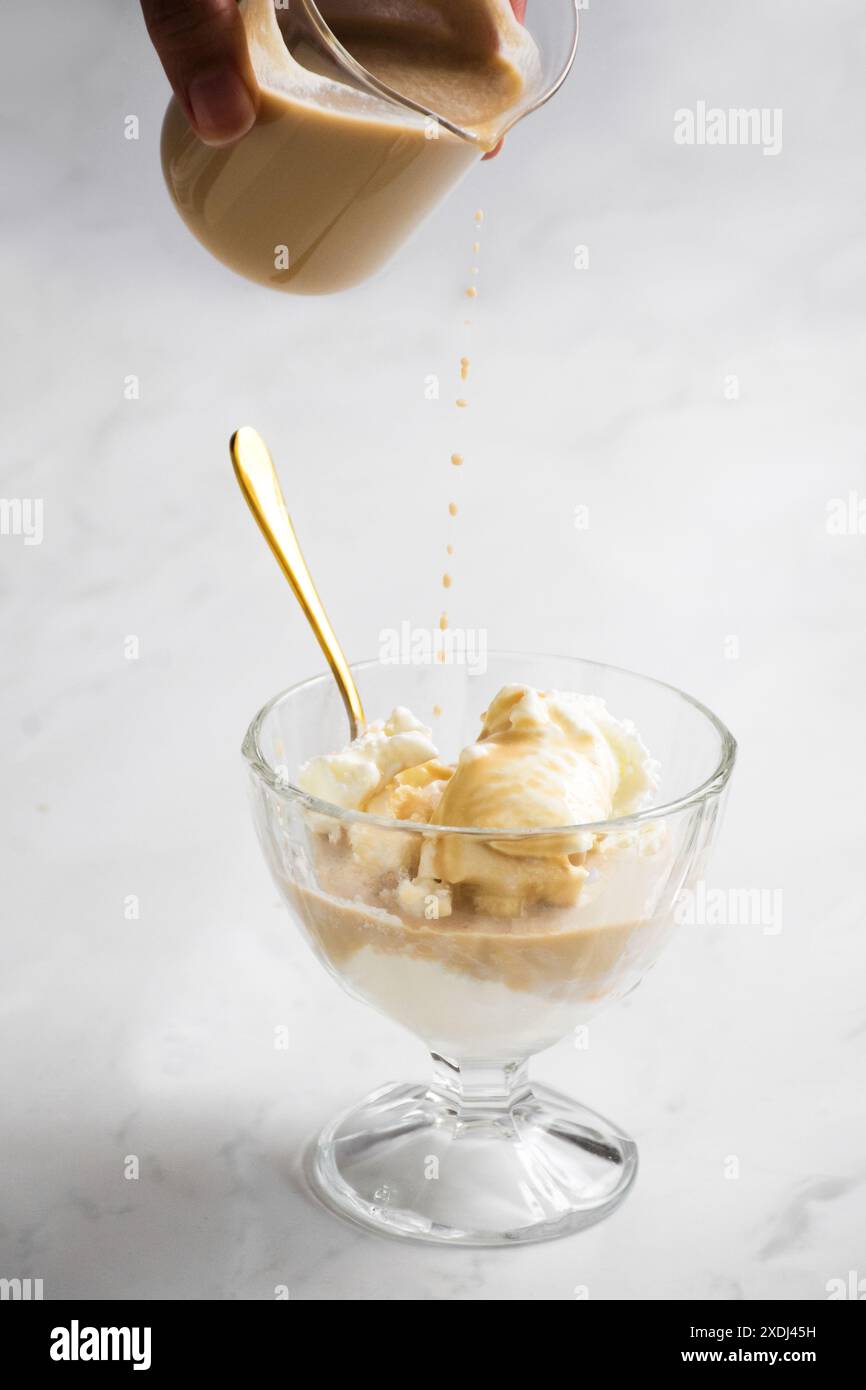 Un primo piano verticale di affogato preparato con espresso versato su gelato alla vaniglia in una tazza di vetro su sfondo bianco Foto Stock