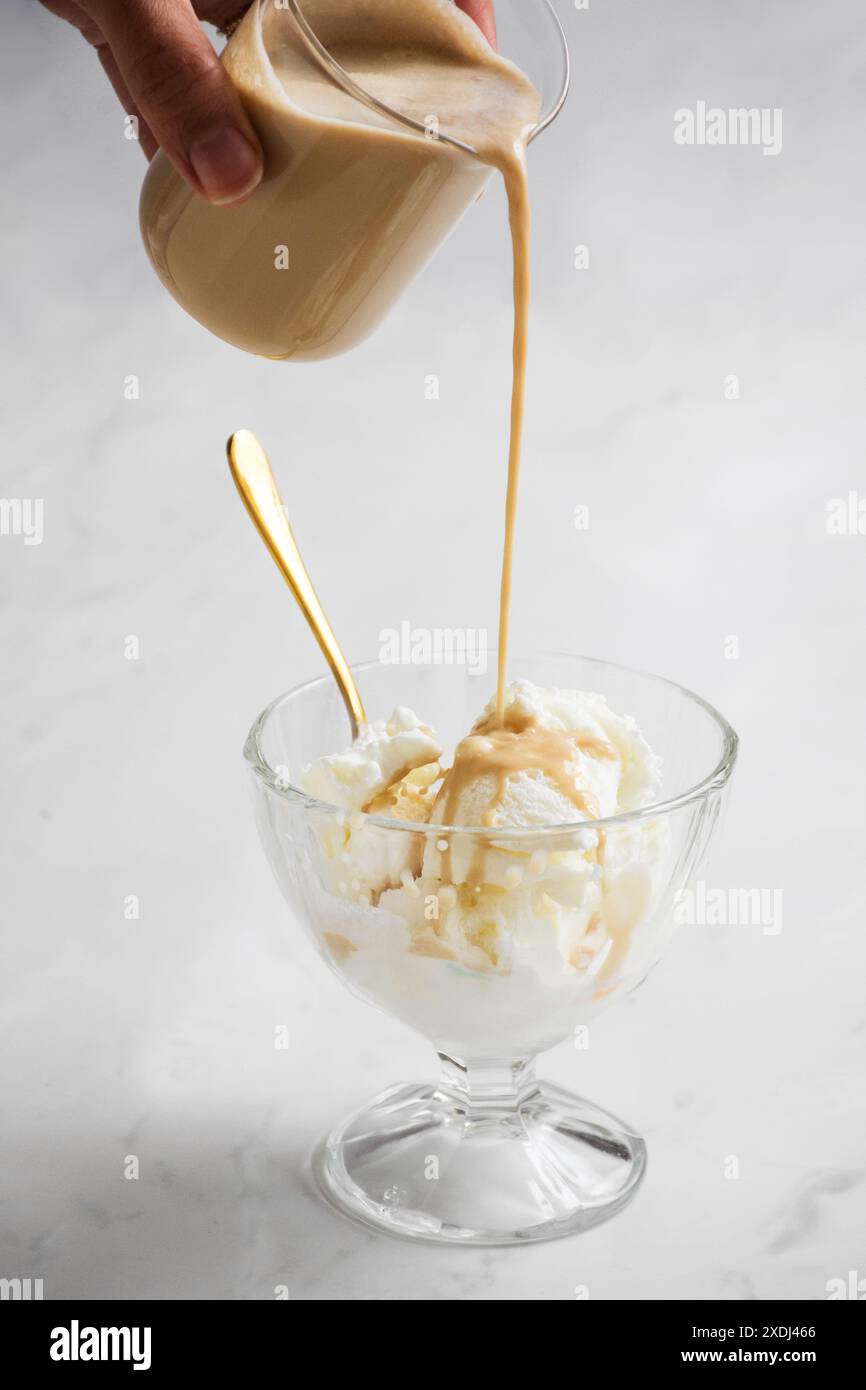 Un primo piano verticale di affogato preparato con espresso versato su gelato alla vaniglia in una tazza di vetro su sfondo bianco Foto Stock