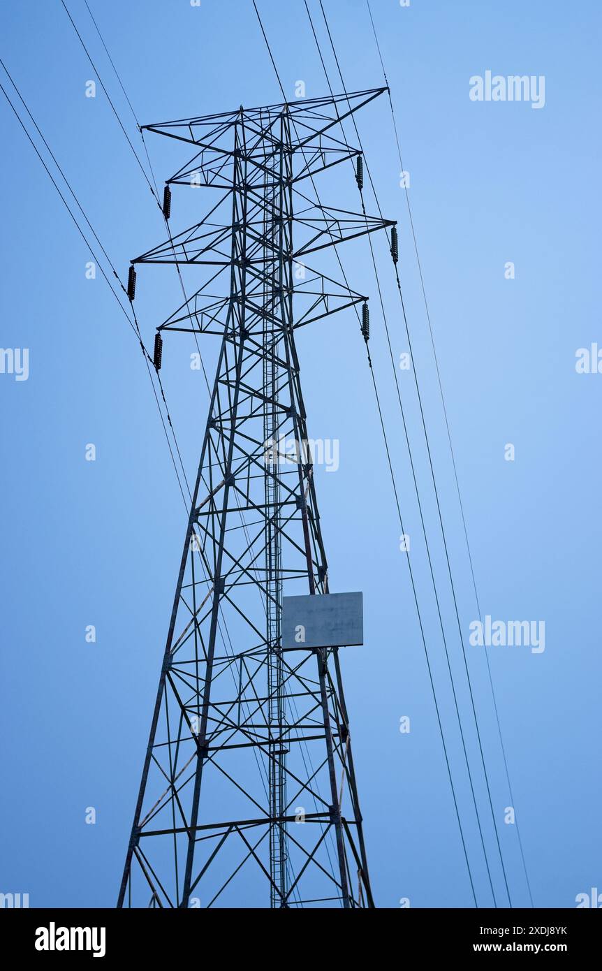 Sagoma di una torre elettrica ad alta tensione contro un cielo blu Foto Stock