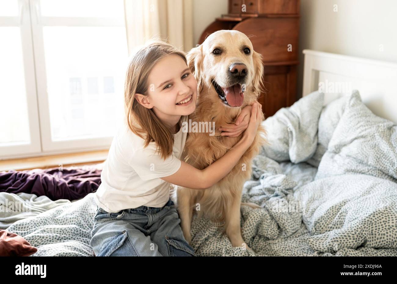 Joyful Little Girl che abbraccia Golden Retriever Dog e guarda la Cameara Foto Stock