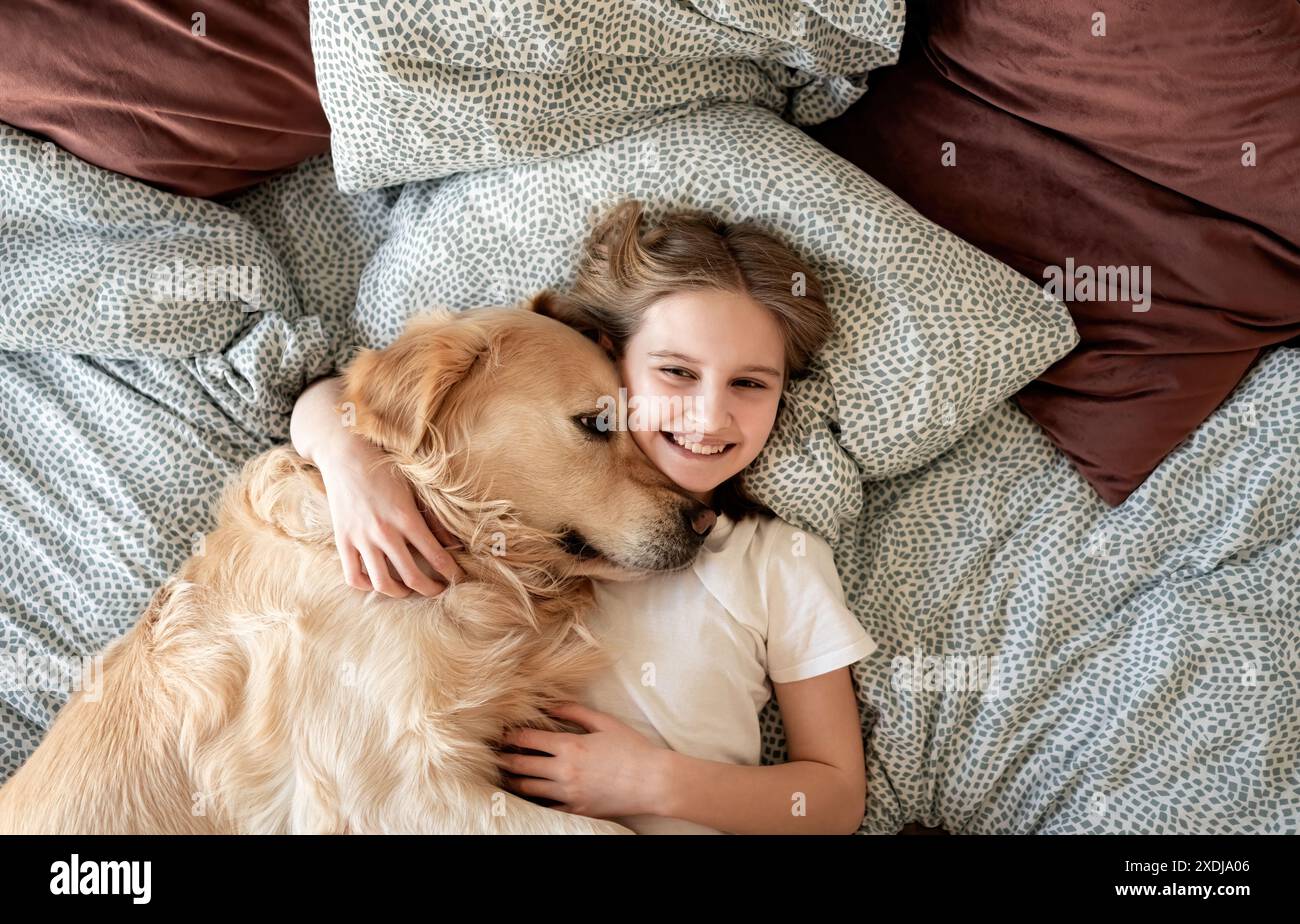 La bambina felice abbraccia il cane e sorride sdraiata su Un letto Foto Stock