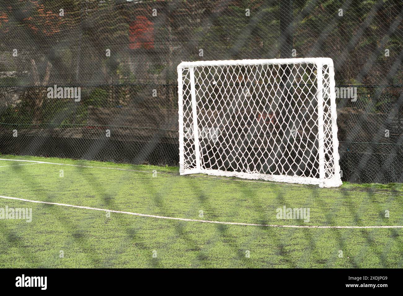 Un gol da calcio vuoto su un campo di erba artificiale verde, con una recinzione a rete in primo piano. Foto Stock