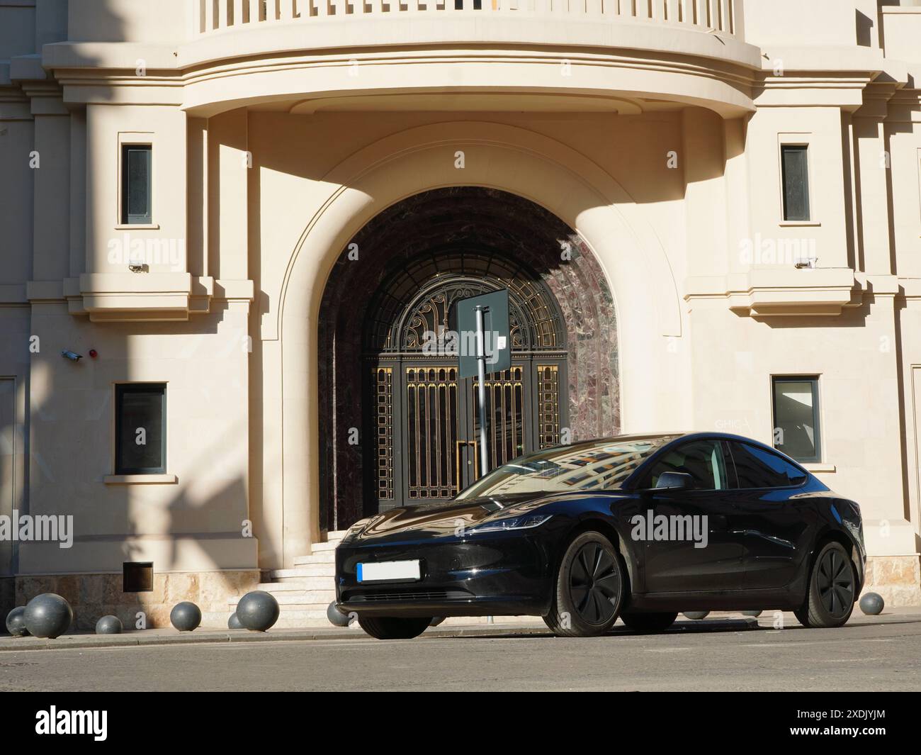 Bucarest, Romania - 16 maggio 2024: Auto elettrica Tesla parcheggiata di fronte all'ingresso dell'edificio istituzionale con una splendida e imponente porta nel centro storico di Bu Foto Stock