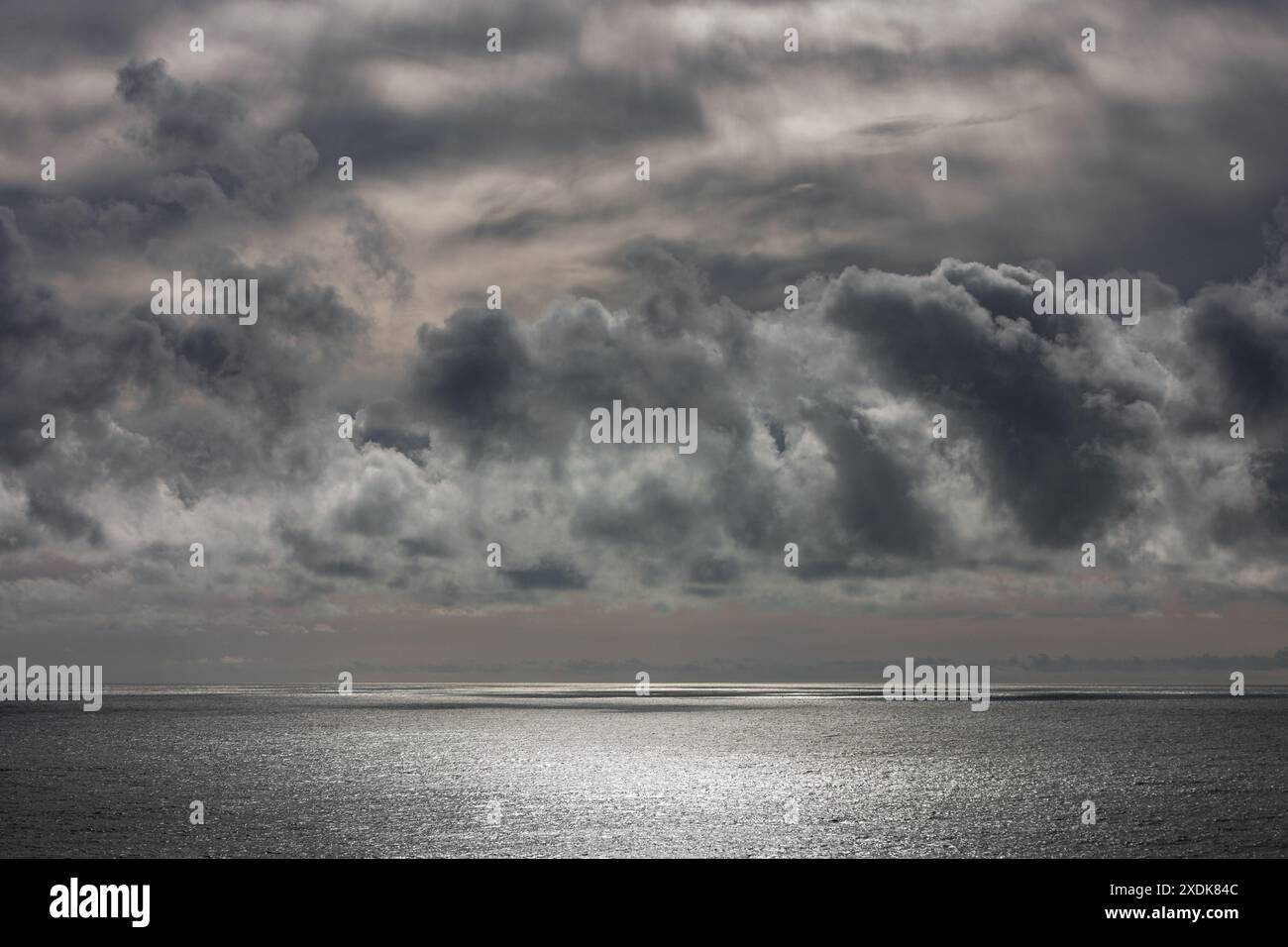 Prima di una tempesta, queste incredibili nuvole si sono formate sul mare. I raggi del sole passano attraverso di loro ma non sono in grado di cambiare il colore grigio del mare Foto Stock