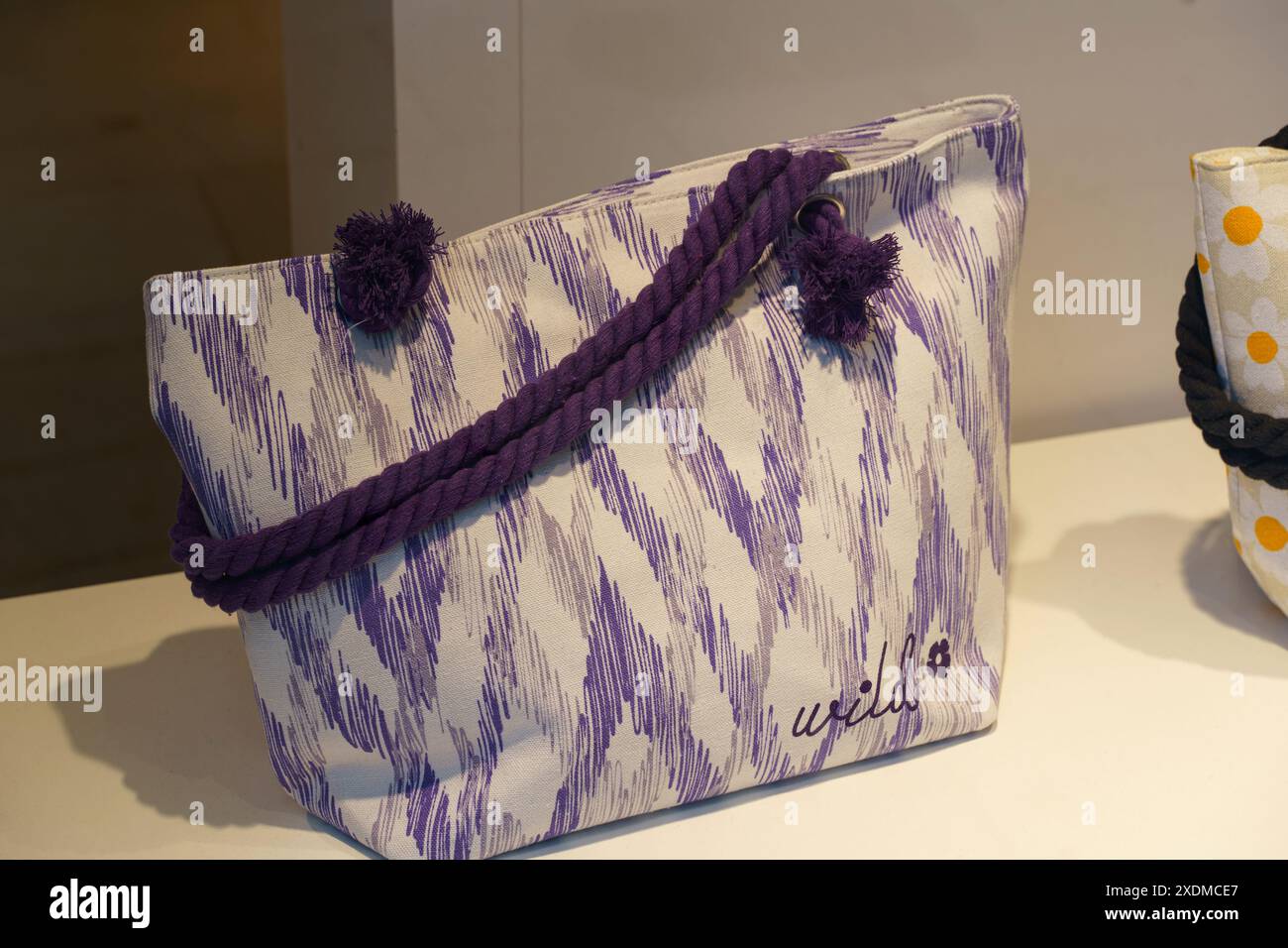 Figueres, Spagna - 14 maggio 2023: Una borsa viola e bianca è posizionata sopra un tavolo di legno in una sala ben illuminata, che mostra i colori vivaci e la semplicità Foto Stock