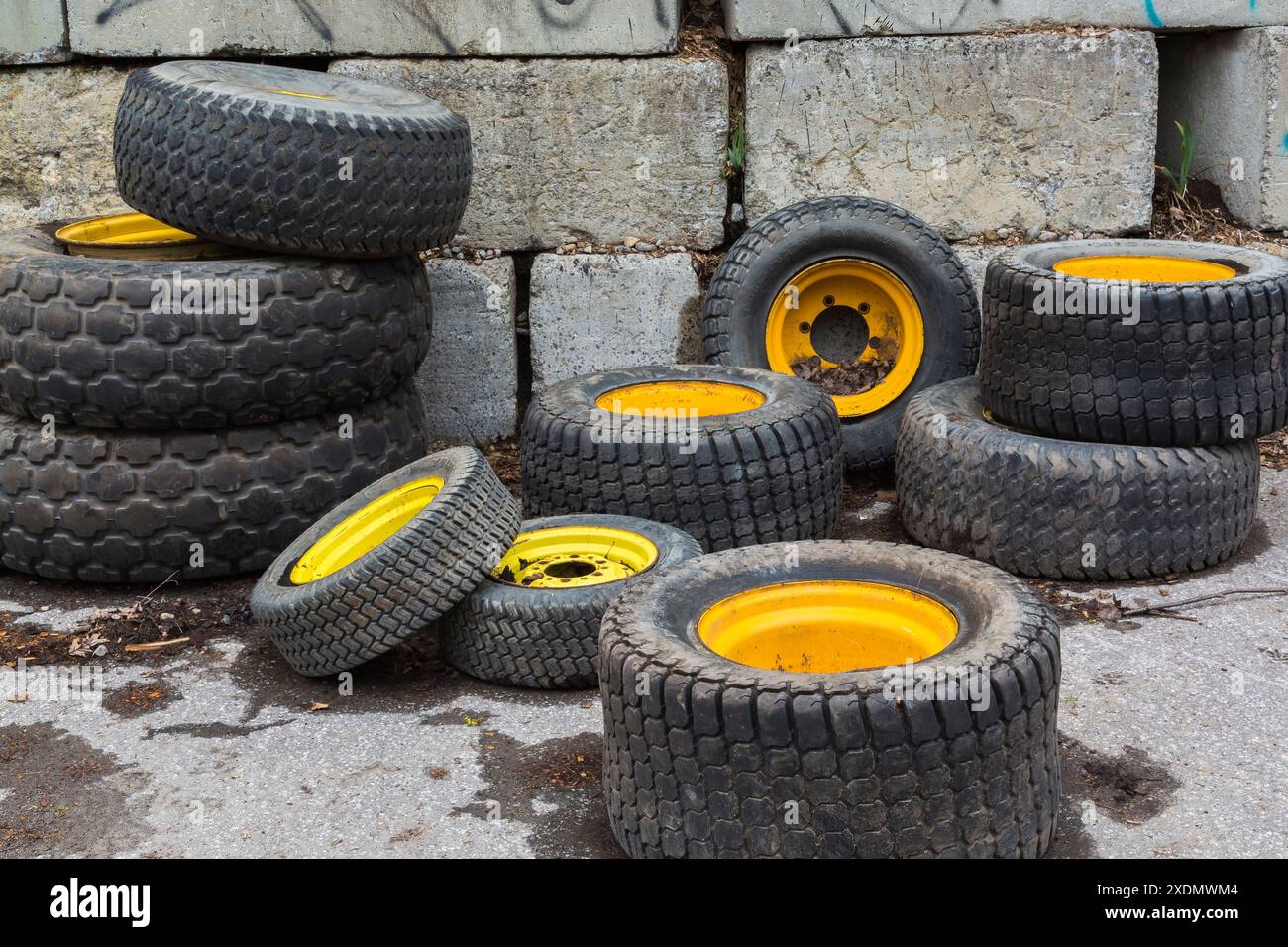 Pneumatici in gomma assortiti per autoveicoli con cerchioni gialli in cestello di cemento presso un deposito di riciclaggio all'aperto. Foto Stock