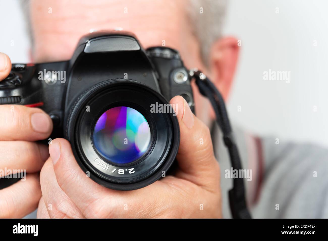 Uno scatto ravvicinato di una persona che tiene in mano una fotocamera digitale con un obiettivo di grandi dimensioni. La fotocamera è messa a fuoco sull'obiettivo, con la sfocatura del volto e del corpo delle persone Foto Stock