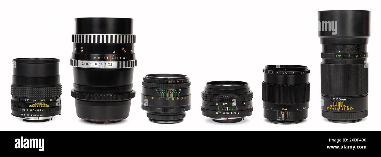 Un gruppo di obiettivi vintage e moderni, dal grandangolo al teleobiettivo, sono disposti in modo ordinato su una superficie bianca. Foto Stock