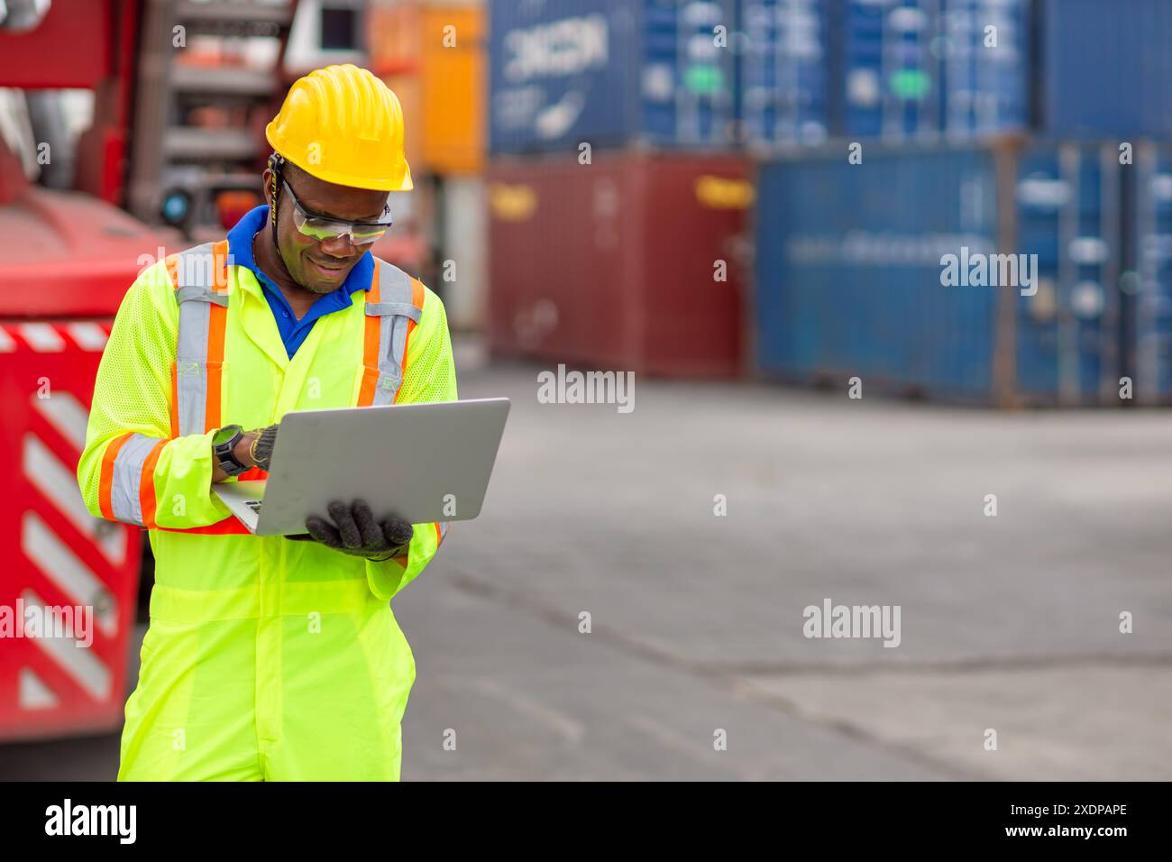 Lavoratore nero africano nel porto di carico Shipping Industrial in Yellow Hard Hat Safety Vest on Duty. Caposquadra o supervisore nel terminal di imbarco delle navi container. Foto Stock