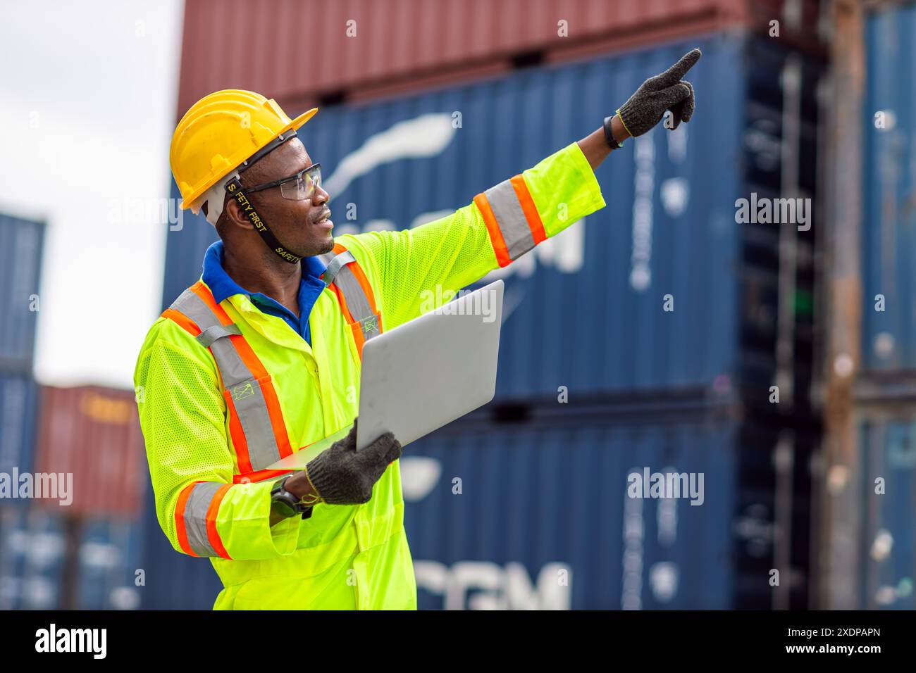 Lavoratore nero africano nel porto di carico Shipping Industrial in Yellow Hard Hat Safety Vest on Duty. Caposquadra o supervisore nel terminal di imbarco delle navi container. Foto Stock