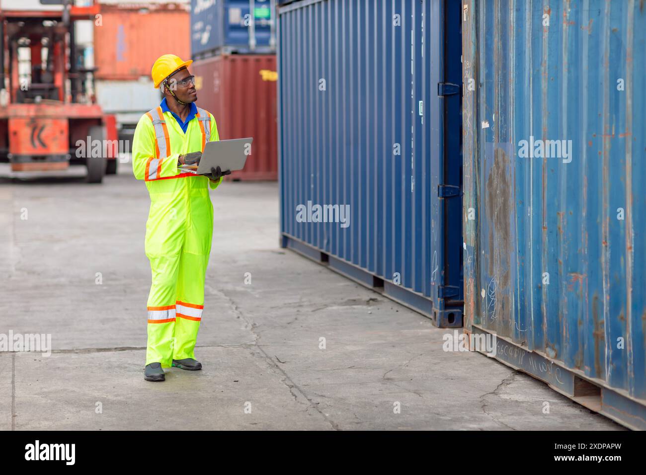 Lavoratore nero africano nel porto di carico Shipping Industrial in Yellow Hard Hat Safety Vest on Duty. Caposquadra o supervisore nel terminal di imbarco delle navi container. Foto Stock