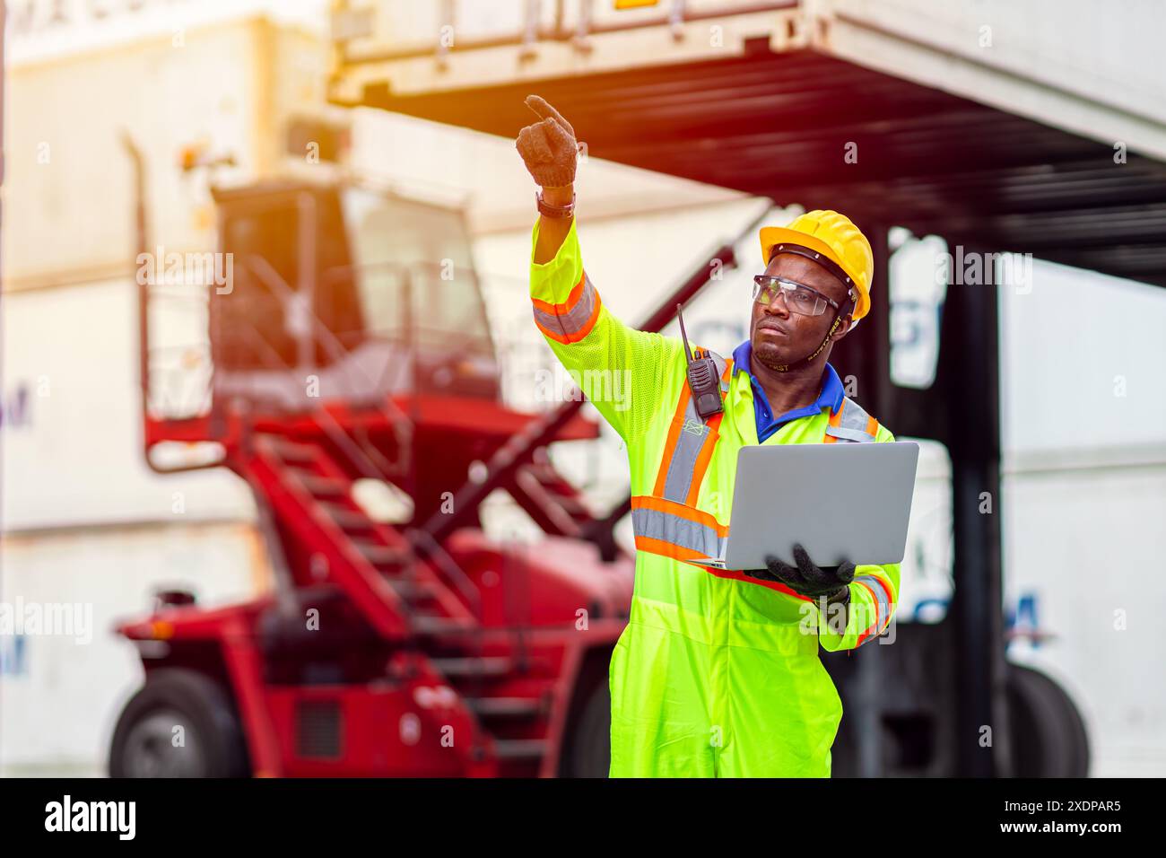 Lavoratore nero africano nel porto di carico Shipping Industrial in Yellow Hard Hat Safety Vest on Duty. Caposquadra o supervisore nel terminal di imbarco delle navi container. Foto Stock