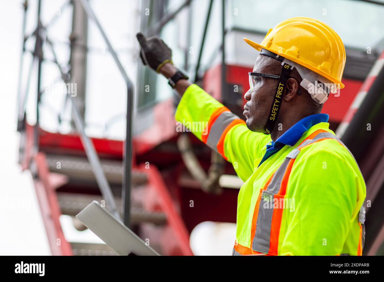 Lavoratore nero africano nel porto di carico Shipping Industrial in Yellow Hard Hat Safety Vest on Duty. Caposquadra o supervisore nel terminal di imbarco delle navi container. Foto Stock